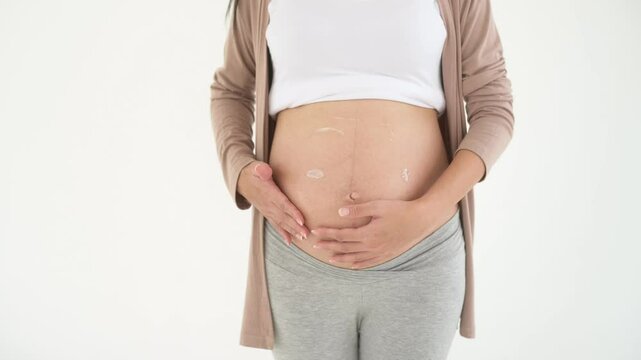 pregnant woman applying moisturizing, stretch mark cream on belly
