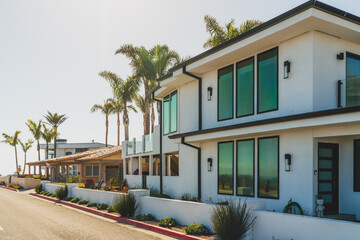 Modern beachfront homes with large windows and palm trees under a clear sky.