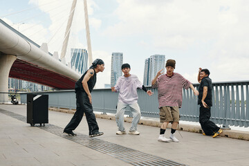 Group of dancers sharing energetic moves on modern urban bridge surrounded by skyscrapers on partly cloudy day, expressing passion for street dance and joy of movement
