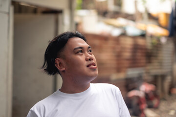 Fototapeta premium An optimistic man looking up while in front of a slum area. A young Filipino residing in an squatter area. Shantytown background.