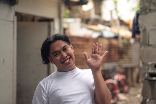 A young chummy gay Filipino man waving hello. A local person living in an squatter area. Slum area background.