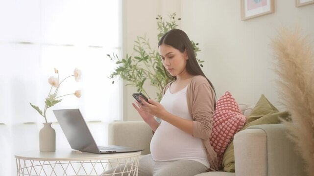Pregnant woman working on laptop and smart phone in the living room at home