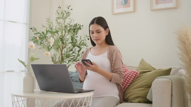 Pregnant woman working on laptop and smart phone in the living room at home