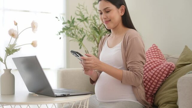 Pregnant woman working on laptop and smart phone in the living room at home
