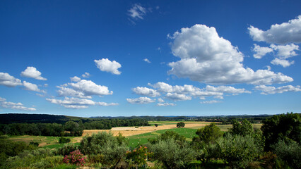 Plaine agricole du sud de la France aux champs cultivés et meules de foins entourés de forêts sosu le ciel bleu et nuageux de la fin de l'été.