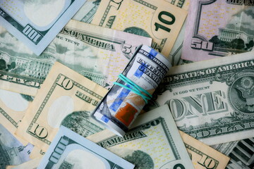 Hundred dollar bills roll lies on big amount of US dollars in different nominations under natural light
