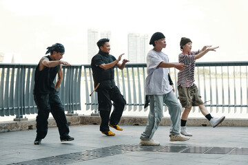 Group of young men engaging in synchronized dance practice outdoors, with urban cityscape in...