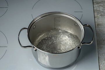 Boiling water in a stainless saucepan on an induction hob. Selective focus.