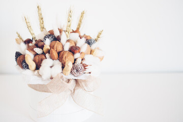 Beautiful handmade Christmas bouquet of nuts, pinecones and cotton flowers in round gift box against white background. Holiday floral decor. Copy space for text.