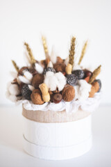 Beautiful handmade Christmas bouquet of nuts, pinecones and cotton flowers in round gift box against white background. Holiday floral decor.