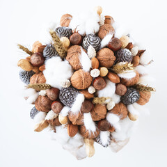 Beautiful handmade Christmas bouquet of nuts, pinecones and cotton flowers, top down view on white background. Holiday floral decor.