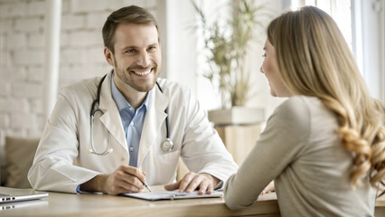 Obraz premium Smiling male doctor in a white coat discussing health with a young female patient in a bright office