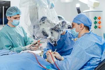 Surgeons conducting a delicate procedure with advanced tools. Two surgeons in blue scrub attire...