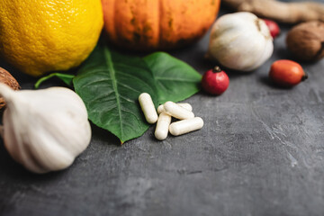 Pharmacy medicine, white capsules and natural immune boost remedies, lemon, garlic, pumpkin, walnuts, dog rose fruit on a dark background
