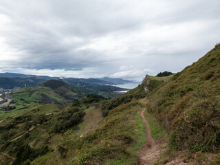 Winding Trail Through Lush Green Hills Overlooking Coastal Valley and Distant Mountains