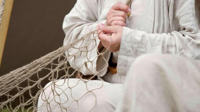 A woman in ancient clothes weaves a net. Craft culture of the Baltics. Historical reenactment. Rumsiskes, Lithuania- 07 05 2024. 