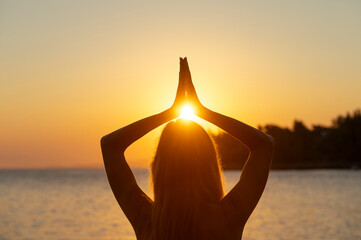 View from behind of a woman with long hair standing by the sea practicing mindfulness and gratitude at sunrise