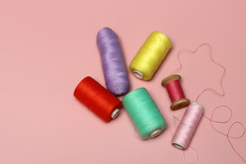 Spools of thread and needles on a pink background with space for text, top view photo of sewing supplies. 