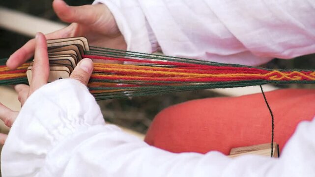 A woman weaves a ribbon using an ancient technique. Craft culture of the Baltics. Historical reenactment. Rumsiskes, Lithuania- 07 05 2024. 