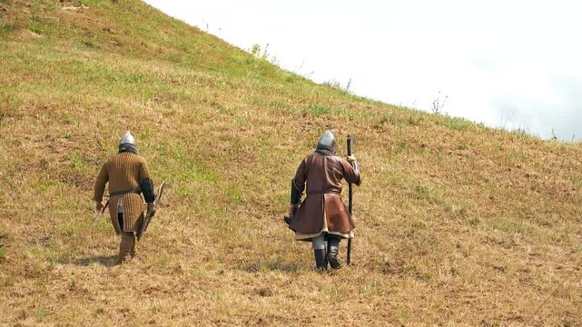 Two men in medieval warrior clothes walk away. Historical reenactment. Rumsiskes, Lithuania- 07 05 2024. 