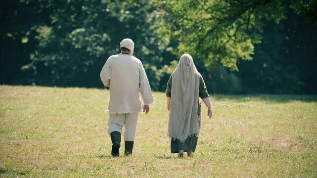 Historical reenactment of baltic tribe. Baltic man and woman with peasant clothes walk away. Rumsiskes, Lithuania- 07 05 2024. 