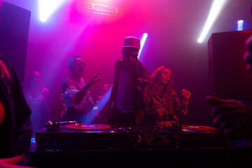 Still footage of a group of young people dancing and jumping while DJ playing the beats