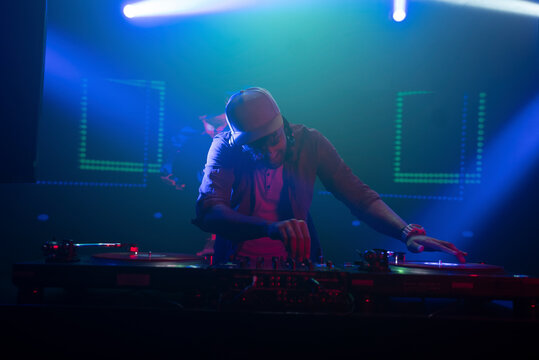 Dj man plays techno music on rave party in club. Disk jokey mixing musical tracks with audio mixer