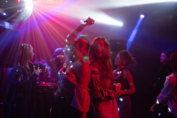 A group of joyful men and women dancing at a nightclub in glowing strobe lights