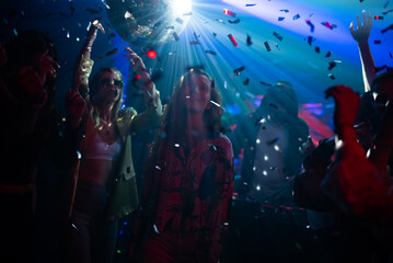 Group of friend celebrating and dancing in night club with illuminated neon night lights and falling confetti