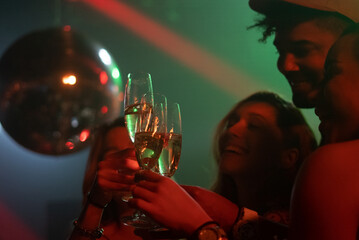 Close-up view of a group of friends clinking glasses filled with alcohol on dance floor
