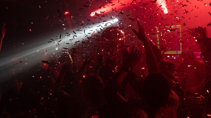 Many happy people partying in nightclub, dancing and enjoying together. Large silver disco ball above the dance floor