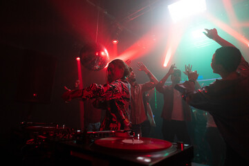 Beautiful Dj woman mixing songs on control panel and crowd dancing in the background