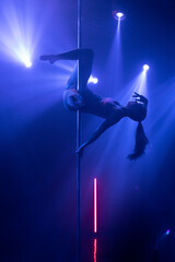 Silhouette of a charming fitness woman exercising on a pole. Exotic dance in a dark studio with...