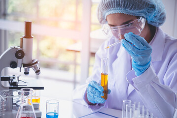 Scientist woman holding chemical test yellow glass tube testing science laboratory. Lab technician holding gold fluid drop to glass tube Urine sample. Asian woman scientist working medical chemistry