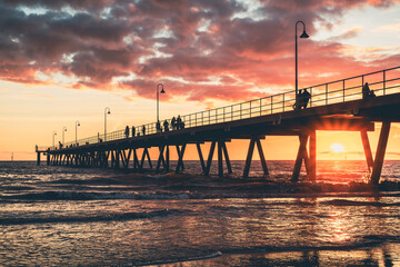 Fototapeta premium Glenelg Beach jetty with people strolling along at sunset, South Australia