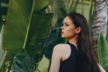 Woman with long black hair standing in front of lush green plants and palm trees on a sunny day