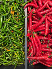 View of a shelf with different types of hot, spicy red and green peppers in a store. Cayenne, chili and jalapeno.