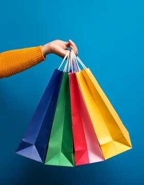 mano de mujer sujetando Bolsas de compras de colores  en un fondo azul de estudio