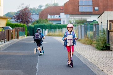 Little happy girl on way to school by pushing scooter. Elementary school child riding in the city,...