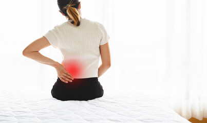 Woman holding her lower back while sitting in bed has chronic back pain. Health Care concept