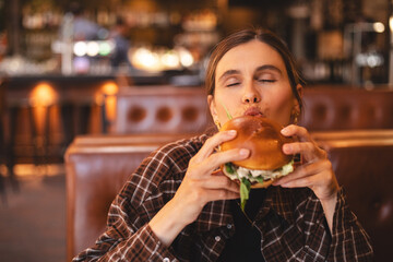 Close-up portrait of a woman in a fast food restaurant eating a hamburger. Hungry woman eating a...