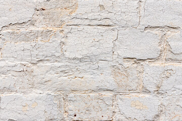 Aged plastered brick wall featuring cracked and peeling cream paint.
