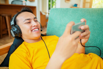 An Indonesian man in a yellow shirt is smiling while playing a video game on his phone
