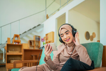 An Arabian Muslim is sitting on a green chair and watching a movie on the mobile phone
