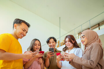 A group of Indonesian people are standing together and looking at their cell phones