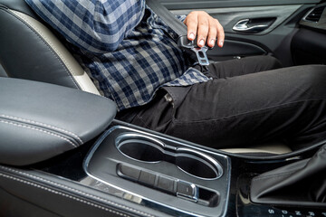 A man is sitting in a car with his hands holding a seatbelt