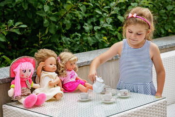 Little preschool girl playing with dolls. Happy excited child play tea party with toys. Role games...