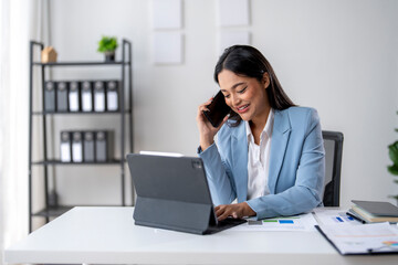 A woman is sitting at a desk and talking on her cell phone
