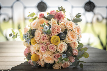 Elegant wedding bouquet with peach and pink roses, yellow craspedia, and greenery, perfect for a romantic bridal arrangement or wedding decor