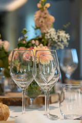 Elegant wine glasses set on a table with soft floral centerpieces in the background. Perfect setting for a wedding reception, romantic dinner, or formal event

